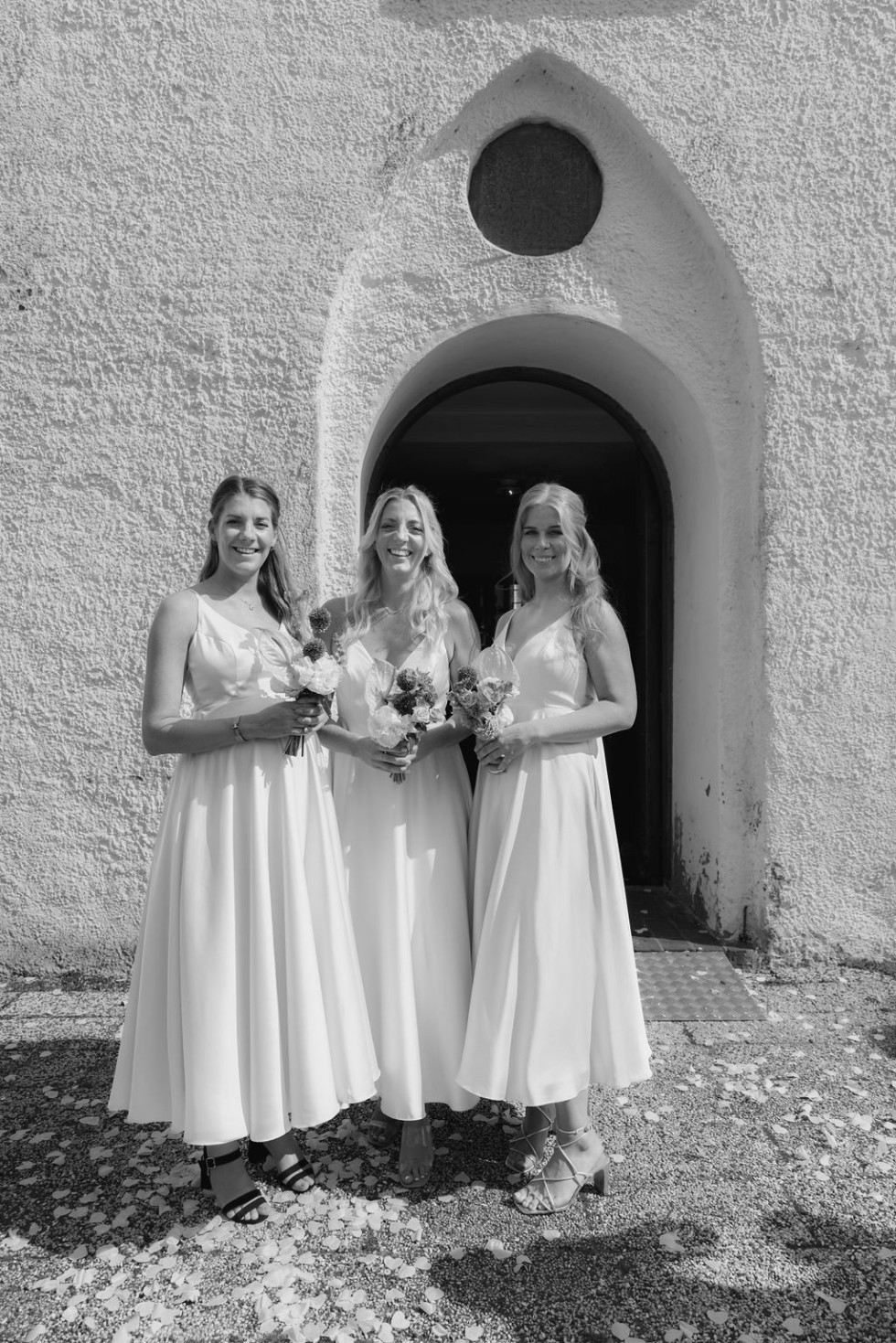 Tre brudtärnor står utanför kyrkan klädda i matchande klänningar, redo för vigseln