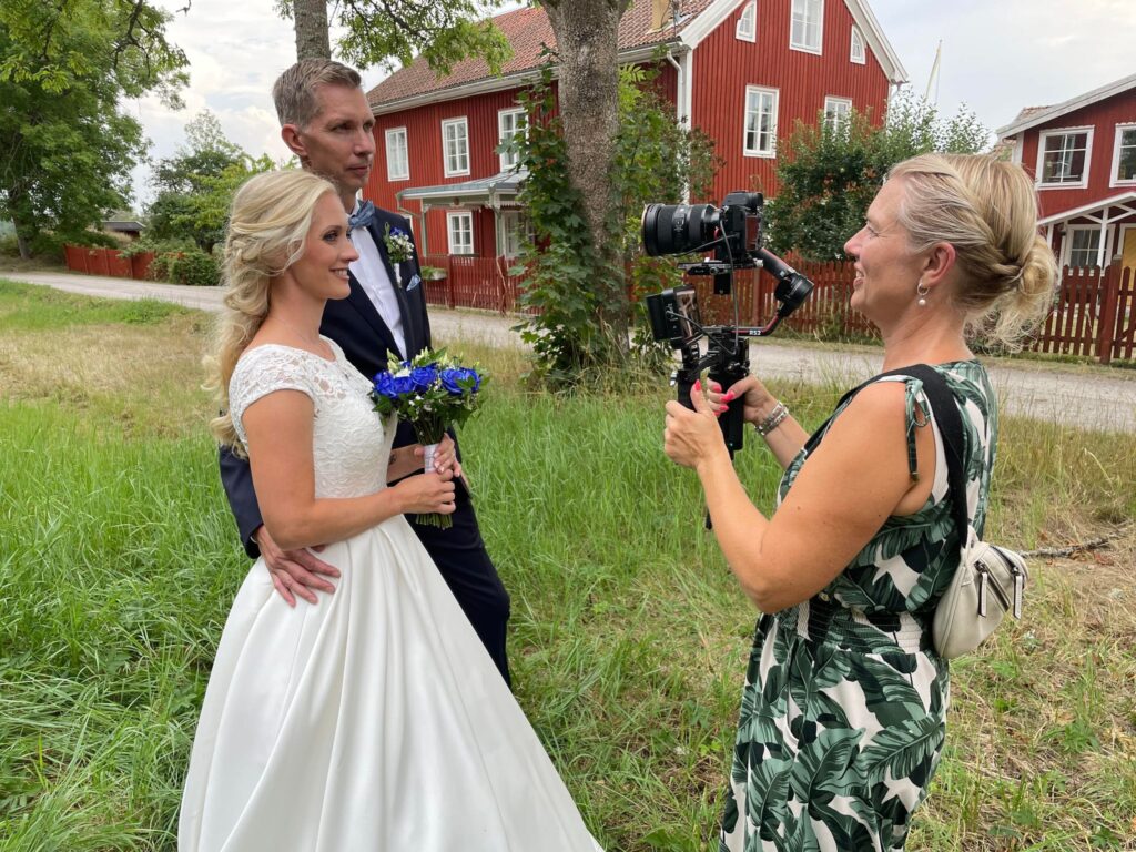 Bröllopsfilm av Videograferna – en fotograf som filmar ett brudpar framför en vacker bakgrund.