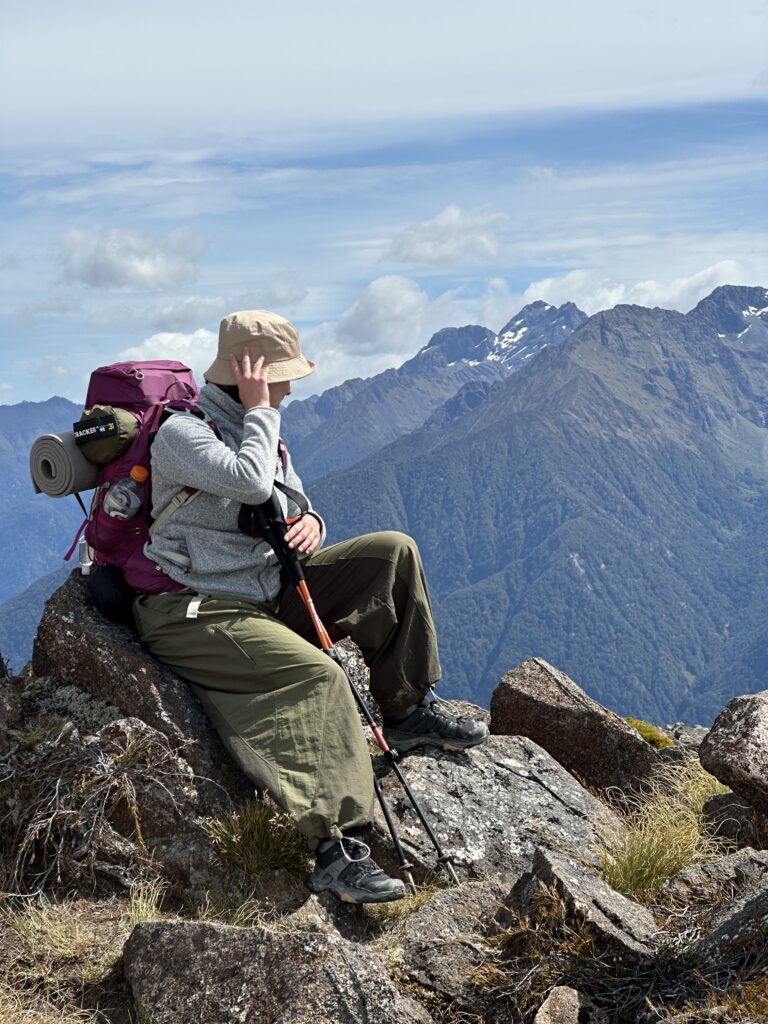 En kvinna som sitter och blickar ut över storslagna berg under sin trekking på bröllopsresan.
